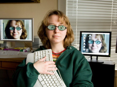 A Female Wears Circuit Glasses in Front of Two Computer Monitors