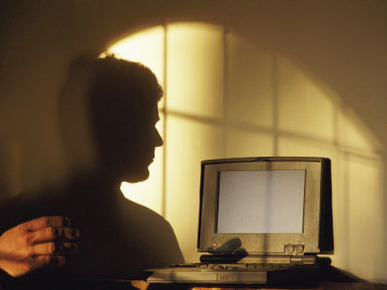 The Shadow of a Man is Projected onto a Wall as He Uses a Computer