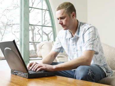 Male Young Adult Sitting on Couch Using Laptop Computer