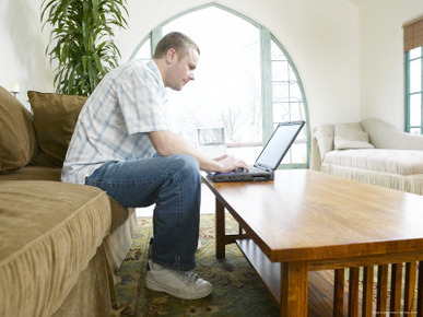Male Young Adult Sitting on Couch Using Laptop Computer