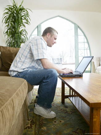 Male Young Adult Sitting on Couch Using Laptop Computer