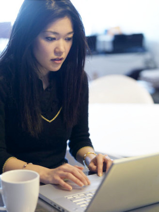 Asian Woman Works on Her Computer in the Morning, Drinking Coffee