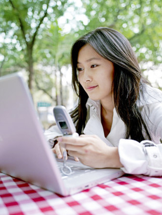 Young Woman Checks Her Laptop Computer with a Mobile Phone in Hand